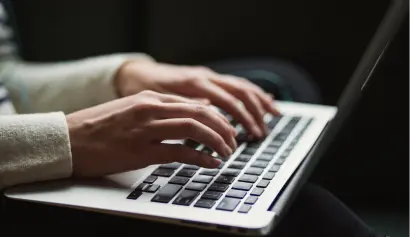 Close-up of a person typing on a laptop with screen is partially visible